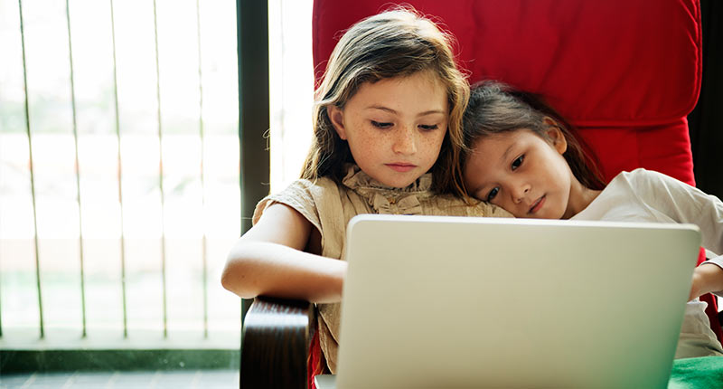 Zwei Mädchen mit Laptop kuscheln sich aneinander